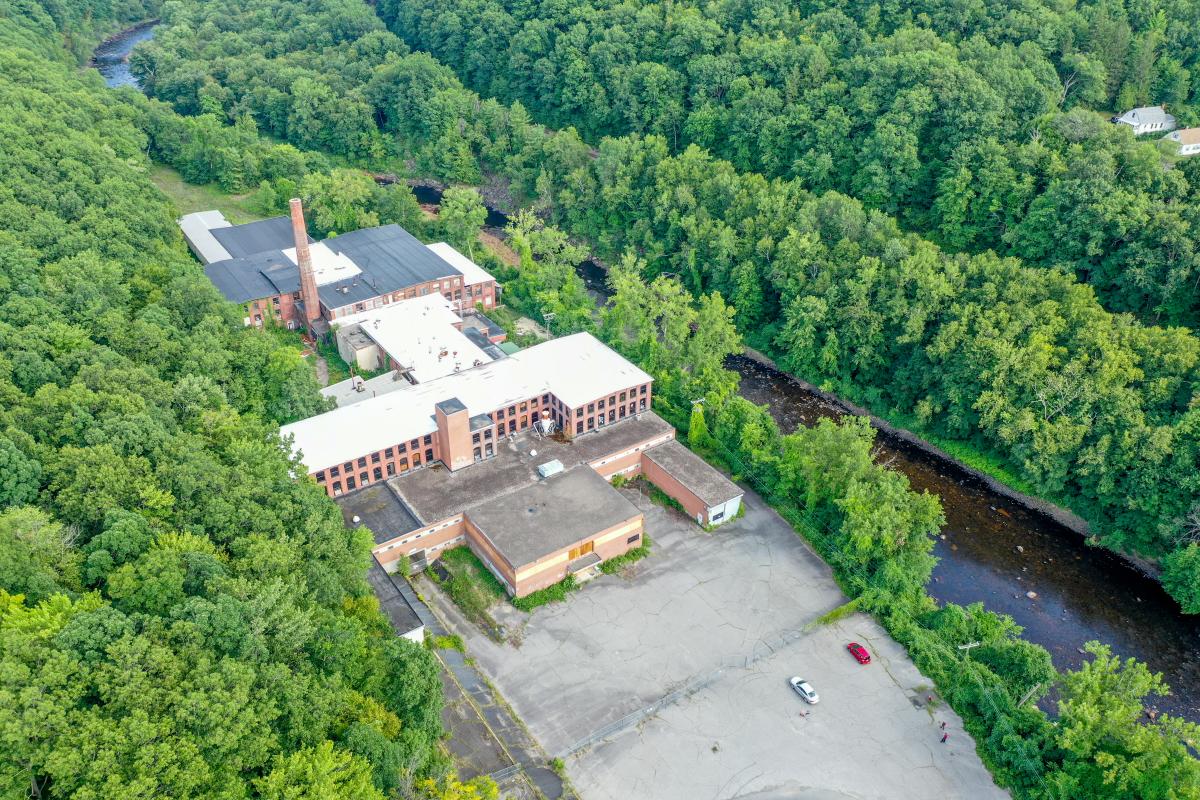 A drone photo of an old factory building along a river surrounded by forest