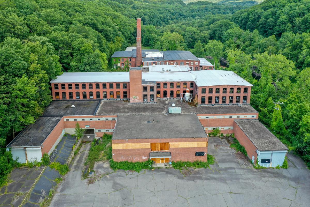 the front of an abandoned mill complex surrounded by green trees