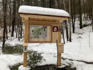 A photograph of a snow covered wood kiosk with a map and several signs